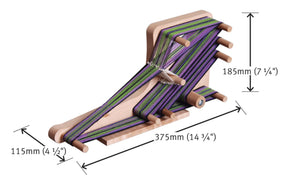 The Ashford Inklette Loom by Ashford Handicrafts Limited is a lightweight wooden loom shown with yarn threaded in green, purple, and black. It features measurements of 185mm (7 1/4") in height, 375mm (14 3/4") in length—ideal for weaving—and 115mm (4 1/2") in width. The loom includes pegs for holding and guiding the yarn.