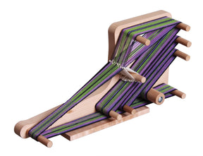 The Ashford Inklette Loom by Ashford Handicrafts Limited is a lightweight wooden loom, threaded with tightly woven green, purple, and black threads. It features multiple pegs to hold the weaving length in place and is set on a flat wooden base with intricate weaving in progress.