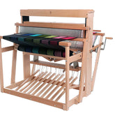 An Ashford 38" Jack Floor Loom Eight Shaft by Ashford Handicrafts Limited, with levers and pedals, showcasing an intricate multi-colored fabric in progress. The multicolored threads form a visually appealing pattern across the loom. Hand cranks and various parts of the loom are visible on either side.