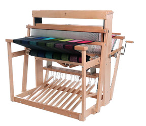 An Ashford 38" Jack Floor Loom Eight Shaft by Ashford Handicrafts Limited, with levers and pedals, showcasing an intricate multi-colored fabric in progress. The multicolored threads form a visually appealing pattern across the loom. Hand cranks and various parts of the loom are visible on either side.