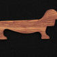 The Dachshund Wiener Dog Weaving Shuttle from Weiner Dog Ranch is a mahogany weaving accessory shaped like a dachshund, showcasing the dog's long body and short legs. Displayed against a plain black background, the visible wood grain adds texture to this handcrafted piece.