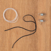 Image of a coil of transparent fishing line, a piece of black string, and two metal springs laid out on a wooden surface, reminiscent of the components you'd find in an Ashford Handicrafts Limited Brake Band Set, Small for E-Spinner 3.