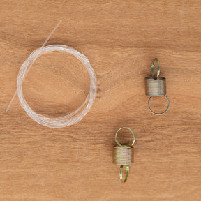 A coil of nylon brake band and two tension springs from the Ashford Brake Band Set by Ashford Handicrafts Limited lie on a wooden surface, reminiscent of the precision found in their spinning wheel systems.