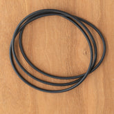 Three black bands from the Ashford Drive Band Set for Ball Winder and O-ring are coiled and overlapping on a wooden surface, making them perfect replacements for your Ashford ball winder.