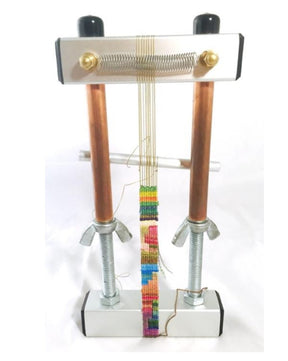 The 5" Mini Mirrix Bead Loom: "Loreli" from Mirrix Tapestry Looms features a rectangular metal frame with two vertical copper rods and large bolts at its base. This loom showcases a rainbow-colored beaded strip in progress, stretched between the rods with thin threads and a coiled spring at the top, making it perfect for experimenting with various warping methods.