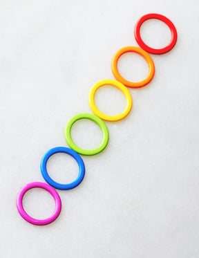 Cocoknits' Colored Ring Stitch Markers feature seven vibrant plastic rings arranged vertically in a gradient from red at the top to purple at the bottom on a light gray background, making them perfect for enhancing your knitting accessories.