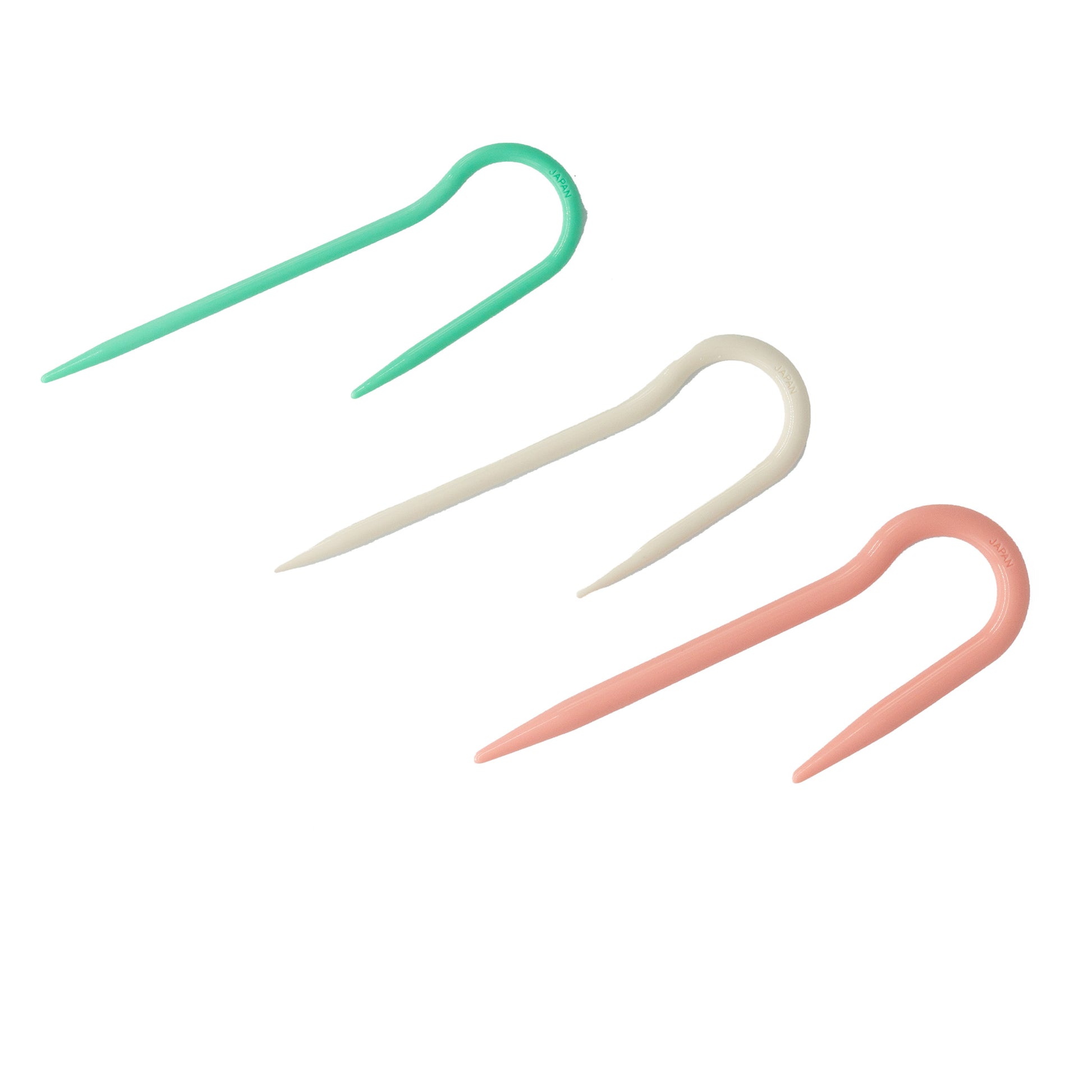 The J-Cable Stitch Holder set of 3 from Bryson Distributing, Inc. includes plastic knitting stitch holders in soft green, white, and pink arranged diagonally. Each holder is U-shaped with pointed ends to securely hold stitches and can be used with cable needles or any needle size 8 projects.