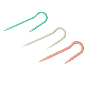 The J-Cable Stitch Holder set of 3 from Bryson Distributing, Inc. includes plastic knitting stitch holders in soft green, white, and pink arranged diagonally. Each holder is U-shaped with pointed ends to securely hold stitches and can be used with cable needles or any needle size 8 projects.