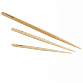 Three Jumbo Bamboo Blunt Needles from Accessories Unlimited, each of different sizes, are arranged diagonally from top left to bottom right on a white background. Each needle features a long, slender body with a tapered tip and a rectangular cutout near the top. The wood color varies from light to medium brown.