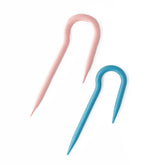 The Jumbo U Cable Stitch Holder by Bryson Distributing, Inc. is showcased on a white background. This set includes two yarn needles, featuring one in pink and the other in blue, both designed with a U-shaped curve at one end and a pointed tip at the other. These are ideal for size 15-19 needles and make an excellent addition to any knitting accessory collection.