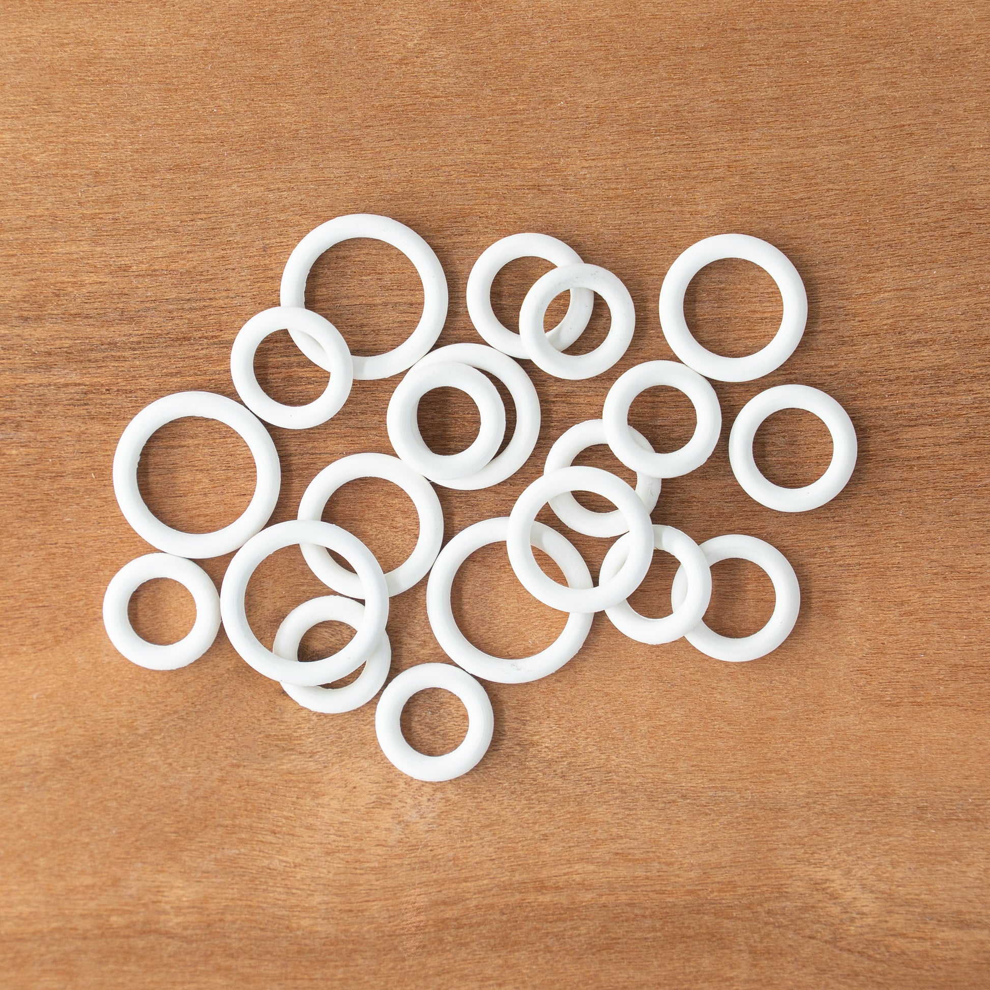 A variety of Bryson Rubber Ring Markers from Bryson Distributing, Inc. in assorted small sizes is scattered on a wooden surface.