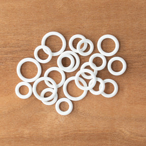 A variety of Bryson Rubber Ring Markers from Bryson Distributing, Inc. in assorted small sizes is scattered on a wooden surface.