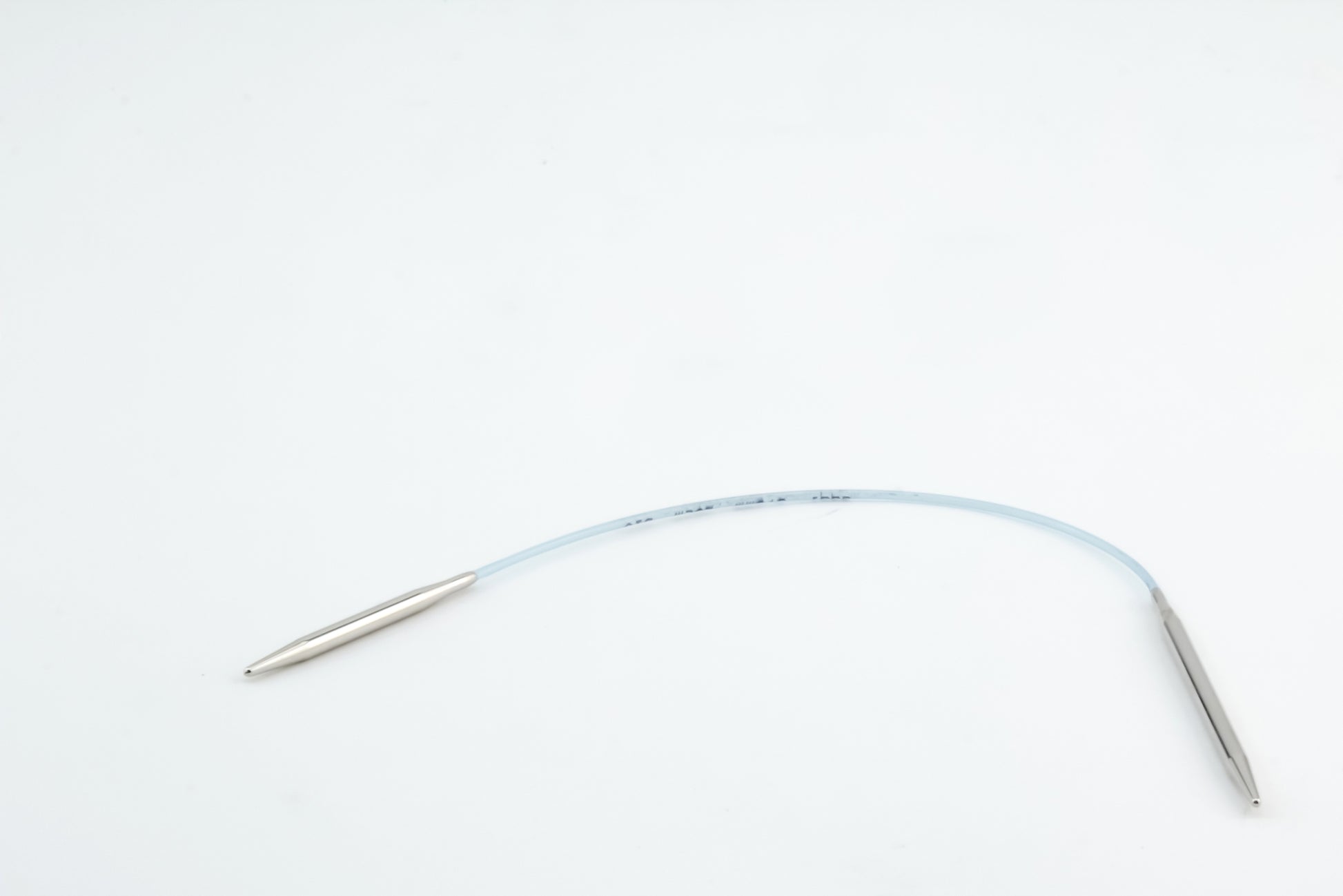 On a white background, the Addi EasyKnit Turbo Circular Needles by Skacel are displayed, featuring a flexible, clear tube connecting two cylindrical metal ends. The sleek tube, reminiscent of a medical device in design, has markings and measurements inscribed on it.