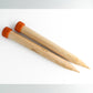 Two large Basix Jumbo Single-Point Knitting Needles, 14" by Accessories Unlimited, with light-colored wooden bodies and orange caps are laid parallel to each other on a white surface. These single-point needles have a diameter measurement of 35.00 mm printed on them, making them perfect for super bulky knitting projects.