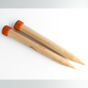 Two large Basix Jumbo Single-Point Knitting Needles, 14" by Accessories Unlimited, with light-colored wooden bodies and orange caps are laid parallel to each other on a white surface. These single-point needles have a diameter measurement of 35.00 mm printed on them, making them perfect for super bulky knitting projects.