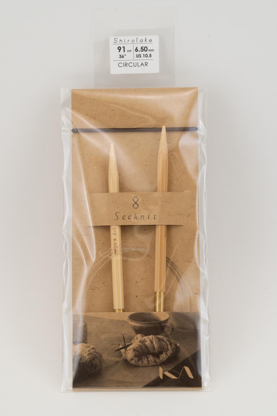 A packaged item from Accessories Unlimited contains two wooden knitting needles labeled "KA Seeknit Shirotake" and connected by a clear cord, indicating they are Circular Bamboo Knitting Needles. The packaging highlights "Shirotake," "91 cm," "6.50 mm," and "US 10.5." At the bottom, a small illustration features yarn and a knitted project, making it ideal for those seeking flexible rotating joints in their knitting tools.