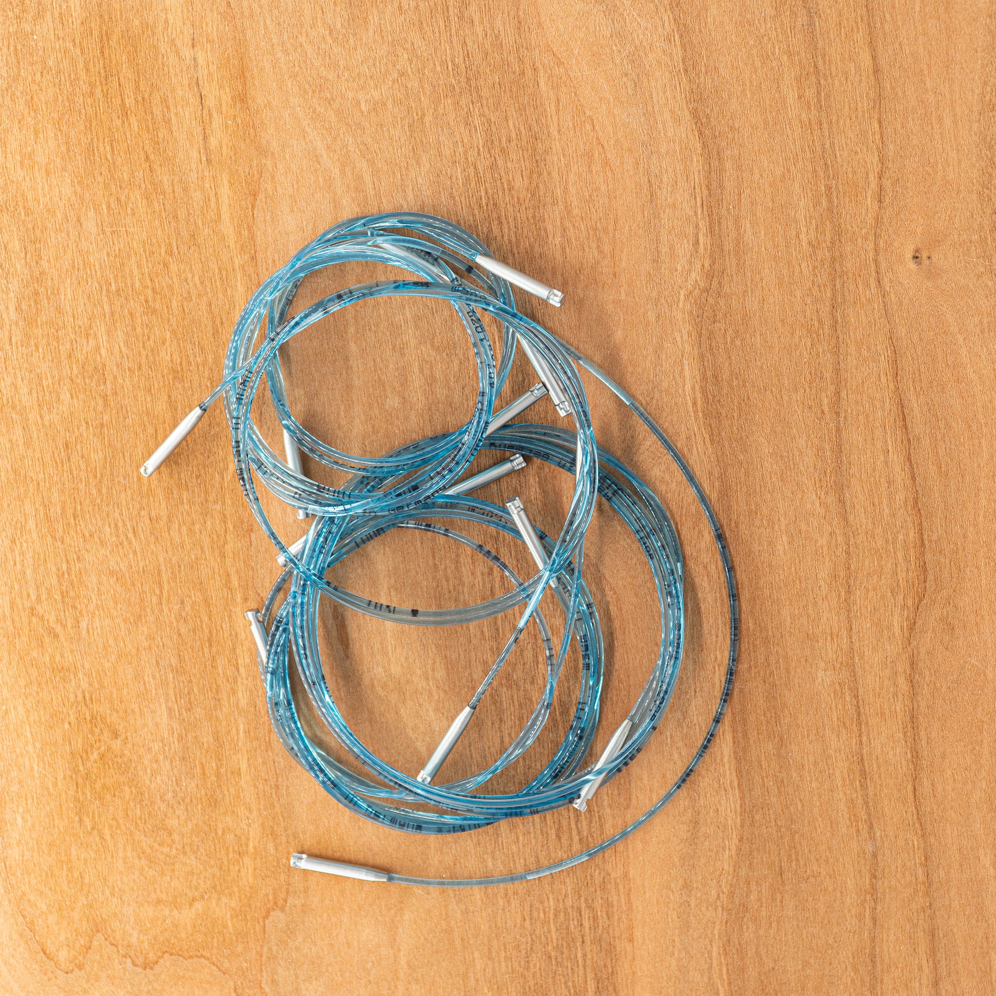 A blue, coiled cable featuring silver connectors, reminiscent of those in the Addi-Click Cord Pack by Skacel, is displayed on a light wooden surface.