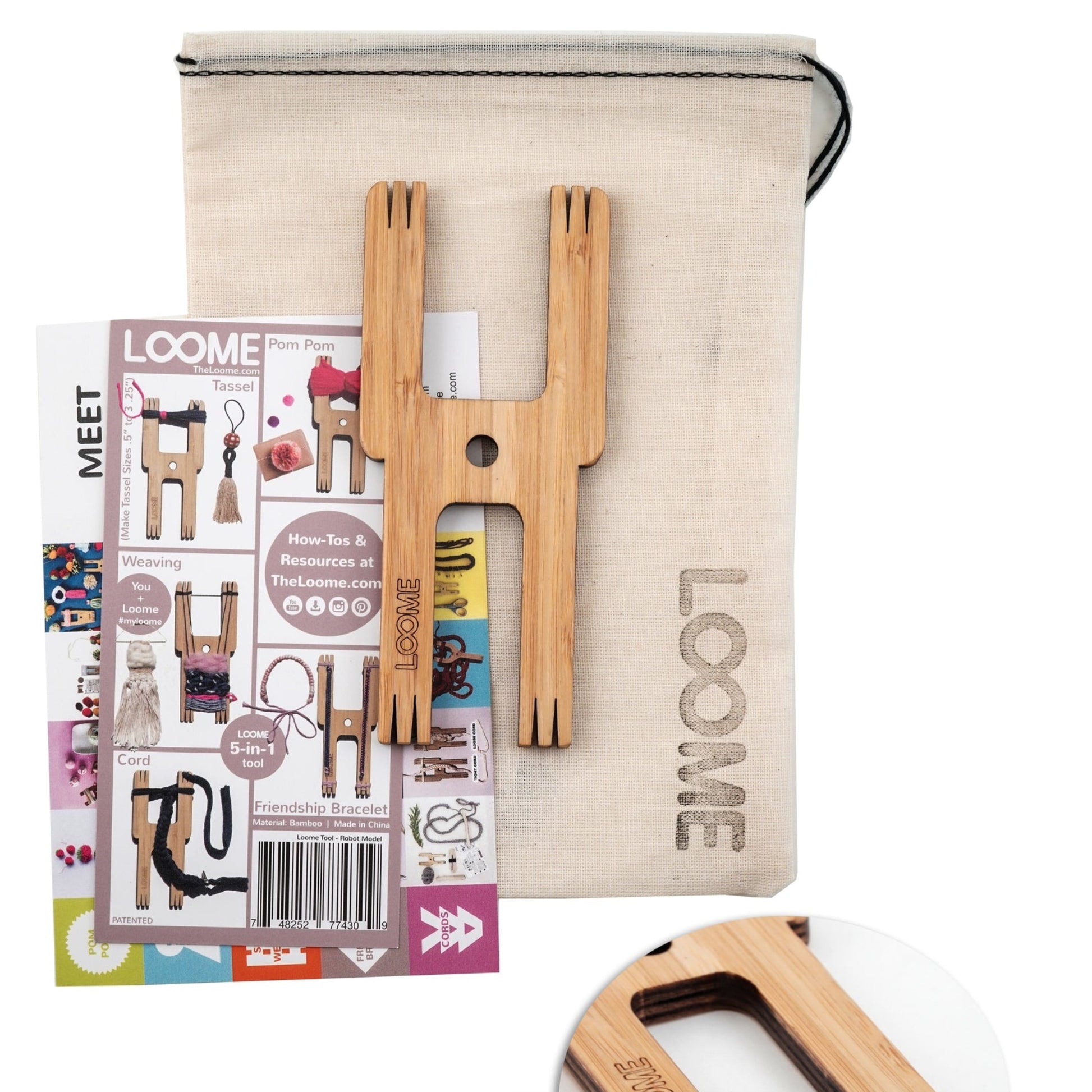 The Loome Tool - Robot Model with Muslin Bag from the brand Loome is a comprehensive crafting kit that includes an all-in-one fiber craft tool, printed instructions, and a fabric bag. The wooden tool features multiple prongs and holes perfect for making pom poms. The beige muslin bag with a drawstring proudly displays the word "LOOME.