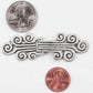 An ornate Antique Silver Metal Clasp from Products from Abroad, featuring intricate swirling designs, is positioned on a white background. For scale reference, a U.S. quarter is placed above and a penny below the embellishment.