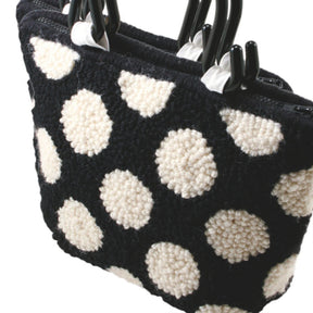 A close-up of the Southern Hills Designs Polka Dot Purse, showcasing its monk's cloth texture with a black background and large white polka dots. The purse is adorned with sturdy, black handles and covered in a soft, wool-like material.