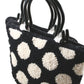 The Polka Dot Purse by Southern Hills Designs is a black tote bag with two black handles, featuring a white polka dot pattern reminiscent of classic Halcyon Rug Wool designs. The bag showcases a textured, woven appearance, with raised dots that provide a three-dimensional look against the plain white background.