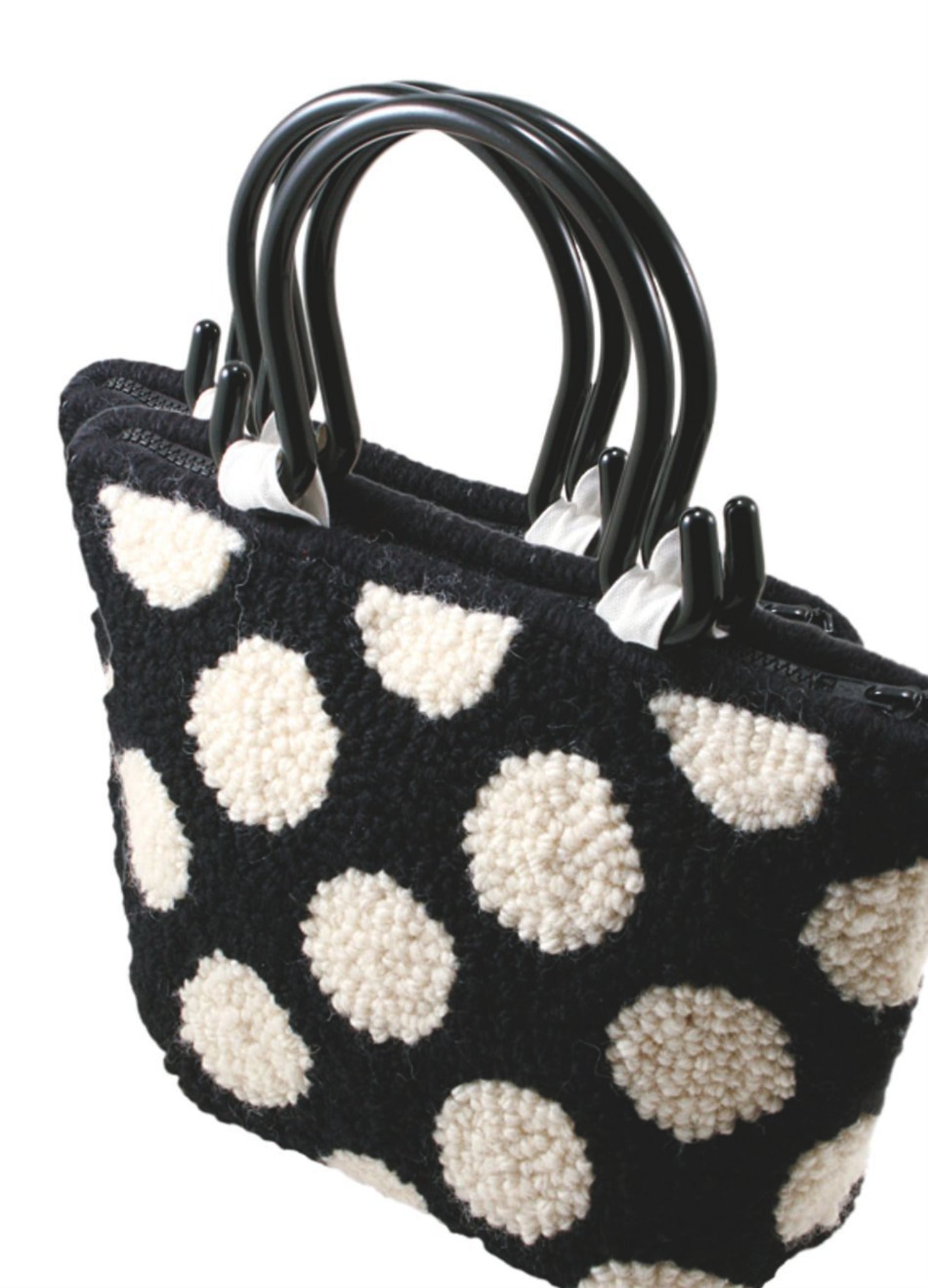 The Polka Dot Purse by Southern Hills Designs is a black tote bag with two black handles, featuring a white polka dot pattern reminiscent of classic Halcyon Rug Wool designs. The bag showcases a textured, woven appearance, with raised dots that provide a three-dimensional look against the plain white background.