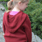 A young girl with blonde hair tied in a ponytail is standing with her back to the camera, wearing Cottage Creations' "A New Generation... Wonderful Wallaby For Kids." The maroon hooded sweatshirt is layered over a pink shirt and paired with blue pants, perfect for kids sizes. She appears to be outside, with green foliage in the background.