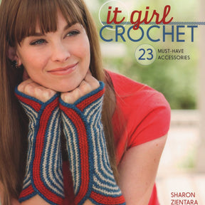 A woman in a red top smiles and rests her chin on her hands, showcasing blue, red, and gray crocheted fingerless gloves. The book cover displays the title "It Girl Crochet - 23 Must-Have Accessories" by Sharon Zientara, published by Ingram Content, and features elegant shawls and trendy hats.