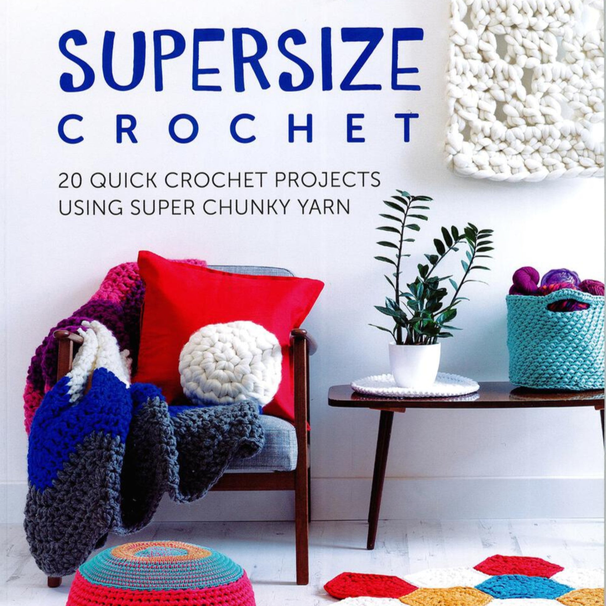 A cozy scene showcasing a crochet book titled "Supersize Crochet - 20 Quick Crochet Projects Using Super Chunky Yarn" by Ingram Content. Various chunky yarn crochet items like blankets, cushions, a plant pot cover, and colorful hexagons are artistically placed in the setup, highlighting oversized home decor.