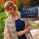 A woman wearing a blue dress poses with an elegant beige crochet shawl draped over her shoulders. The text overlay reads, "Ingram Content Presents Classic Crochet Shawls: 20 Free-Spirited Designs Featuring Lace, Color, and More." Showcasing intricate crochet techniques, she stands outdoors against a softly blurred background.