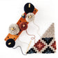 The "Corner to Corner Crochet - 15 Contemporary C2C Projects" by Ingram Content features an elegant wooden holder with five spools of yarn in blue, grey, cream, red, and black. A crochet hook is attached to a partially completed C2C crochet granny square triangle blanket in shades of grey, red, black, and cream—perfect for adding a touch of charm to your home decor.