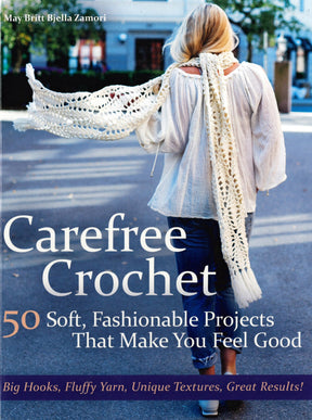 Cover of the book "Carefree Crochet" by May Britt Bjella Zamori, distributed by Ingram Content, illustrates a woman with long blonde hair walking away in a white crocheted shawl. The text reads "50 Soft, Fashionable Projects That Make You Feel Good" and "Big Hooks, Fluffy Yarn, Unique Textures, Great Results!" Embrace wearable crochet!