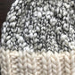 Close-up of a knitted fabric featuring a blend of white and black chunky yarn in the upper section and solid cream yarn in the lower, crafted with luxurious merino wools. The thick texture evokes the cozy charm of an Aguas Blancas Hat Pattern by Kristel Nieves.