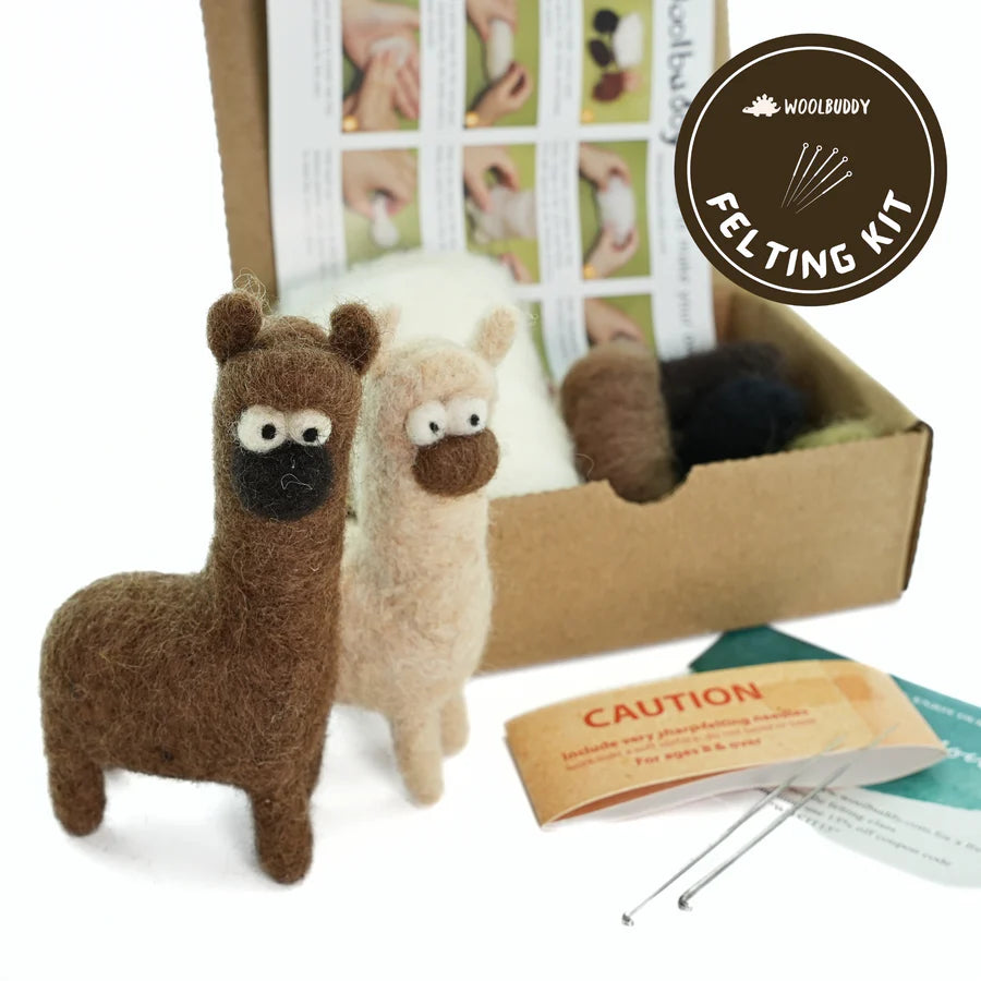 The Woolbuddy Needle Felting Kit is featured, showcasing two needle-felted alpaca figures, one in brown and the other in white. The kit contains wool roving, felting needles, instructions, and a "Caution" card. The Woolbuddy logo is prominently displayed in the top right corner.