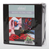 A black Needle Felting Foam Pad, 6 inches square (15cm), in packaging labeled "Ashford Handicrafts Limited." The label features images of creative needle felting projects, such as a hand at work, vibrant felt butterflies, and vivid red flowers. The dimensions are 15cm x 15cm x 5cm.