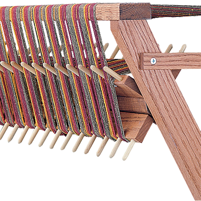 A close-up view of a wooden weaving loom with multicolored threads. The Schacht Sectional Warp Beam for Standard Floor Loom, by Schacht Spindle Co., features evenly spaced pegs, angled supports, and a sectional warp beam, showcasing a traditional crafting tool used for weaving textiles.