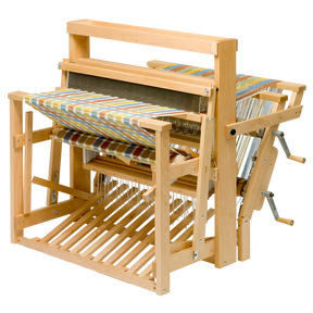 The Schacht Standard Floor Loom Double Back Beam by Schacht Spindle Co. features a partially woven, colorful fabric in progress with an array of vibrant shades. The loom’s detailed mechanics and framework, including the heddles, warp threads, and treadles, are clearly visible. A supplementary warp adds complexity to the piece set against a neutral background.