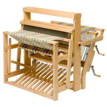 The Schacht Standard Floor Loom Double Back Beam by Schacht Spindle Co. features a partially woven, colorful fabric in progress with an array of vibrant shades. The loom’s detailed mechanics and framework, including the heddles, warp threads, and treadles, are clearly visible. A supplementary warp adds complexity to the piece set against a neutral background.