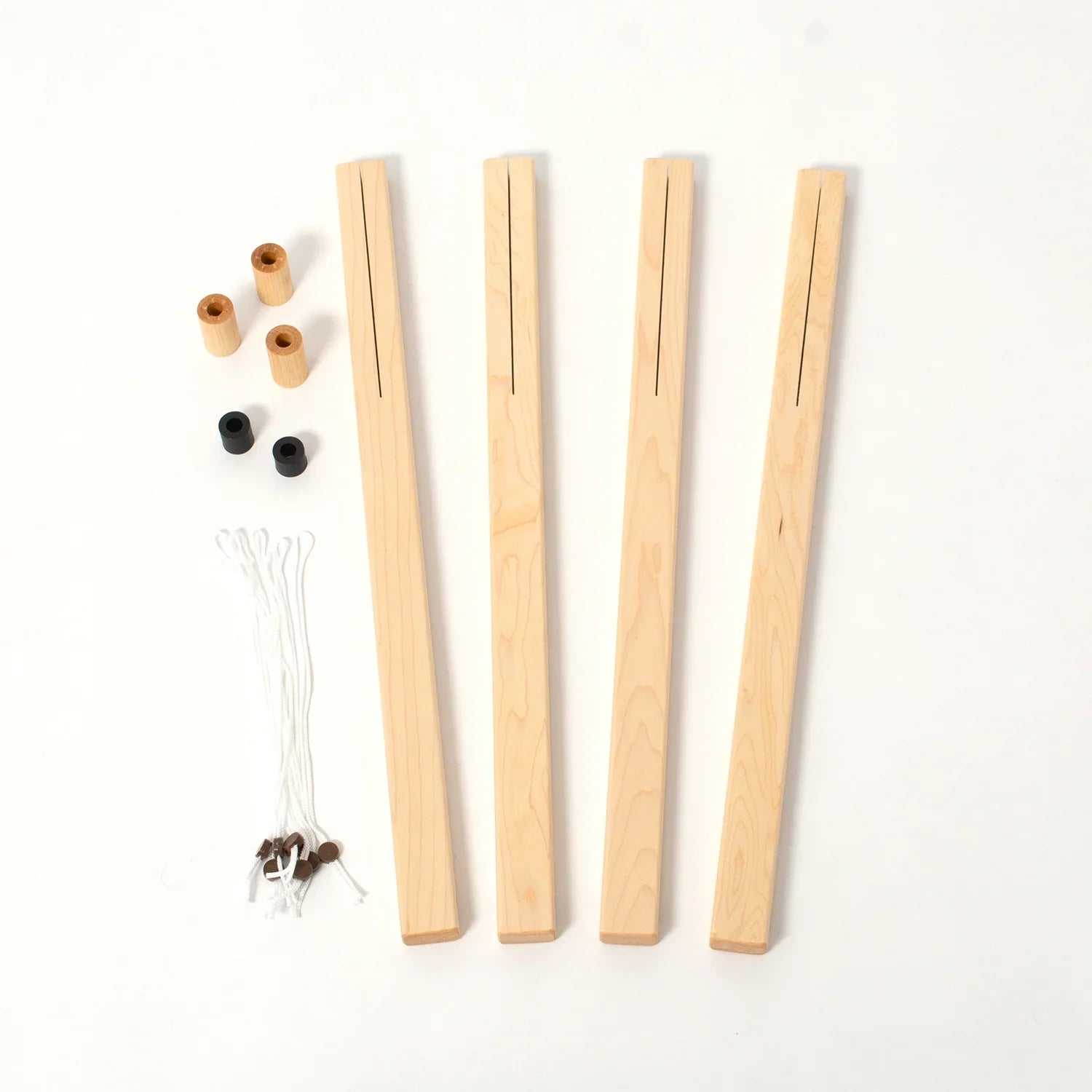 The image showcases the Schacht Spindle Co.'s Schacht Wolf Loom 4-Treadle Add-On Kits, featuring four wooden dowels with slits, four wooden spools, two black spools, and several lengths of white string with attached metal ends. The components are laid out neatly on a white surface to highlight their versatility for complementing the Schacht Wolf Loom add-on treadles.