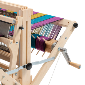 A close-up of a well-crafted Schacht Sectional Warp Beam for Wolf Looms by Schacht Spindle Co. with colorful threads being woven. Various components, including gears, levers, and Sectional Warp Beams in vibrant colors like purple, blue, and yellow, are visible. The loom kit appears highly functional for textile creation.