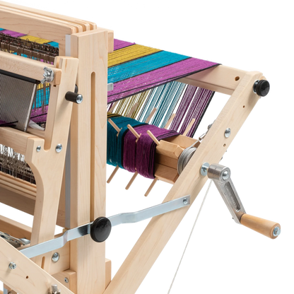 A close-up of a well-crafted Schacht Sectional Warp Beam for Wolf Looms by Schacht Spindle Co. with colorful threads being woven. Various components, including gears, levers, and Sectional Warp Beams in vibrant colors like purple, blue, and yellow, are visible. The loom kit appears highly functional for textile creation.