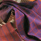 A close-up of two woven fabrics draped over dishes. The top fabric resembles a stylish tablecloth in purple with a red grid pattern, while the bottom one is red with dark blue diagonal stripes. The background showcases neutral-colored dishes in a warm, orange-tinted setting. These beautiful textiles are featured in the "Best of Handwoven Yarn Series: A Dozen Projects in 10/2 Pearl Cotton (Printed Version)" by Long Thread Media.