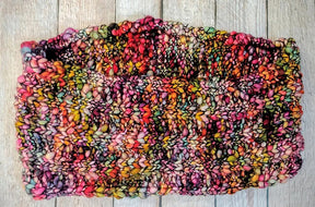 A stunning multicolored knitted scarf made with superwash merino in hues of pink, orange, green, and black is elegantly arranged on a wooden surface, utilizing the Malabrigo Caracol yarn for enhanced texture. This creation is part of the Veinte Cowl Pattern by Kirsten Hipsky.