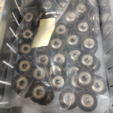 A Louët Hollandia roller replacement kit - 8 shaft from Louët Inc. is organized within a metal bin, containing numerous small black and silver ball bearings, some of which are in a clear plastic bag. Among them are 32mm rollers with visible inner rings. A partially visible yellow piece of paper is inside the bag.