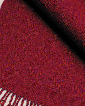 A close-up of the Best of Handwoven Yarn Series: A Dozen Projects in 10/2 Pearl Cotton (Printed Version) by Long Thread Media displays a red and purple woven tablecloth with intricate star-shaped patterns. The textile has a rich texture and includes fringe details at the edge. The vibrant colors and detailed weaving highlight the craftsmanship of this exquisite fabric.