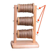 The Ashford Lazy Kate Wire - Packaged 3pc by Ashford Handicrafts Limited includes a wooden thread rack resembling a Horizontal Lazy Kate, holding three spools of brown twine arranged vertically. Red arrows point towards the ends of the spools on the right side. The rack features a simple base and two vertical supports.