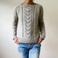 A person wearing the Avalanche Pullover Sweater Pattern by Heidi Kirrmaier, featuring a chevron design on the front, along with blue jeans, stands against a plain background with their hands tucked in their jeans pockets.