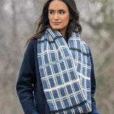 Wrapped in the Blue Sky Fibers Aurora Infinity Cowl, a person stands outdoors. The natural woolly warmth of the cowl complements their dark blue coat and long dark hair, while softly blurred trees form the backdrop.