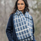 Wrapped in the Blue Sky Fibers Aurora Infinity Cowl, a person stands outdoors. The natural woolly warmth of the cowl complements their dark blue coat and long dark hair, while softly blurred trees form the backdrop.