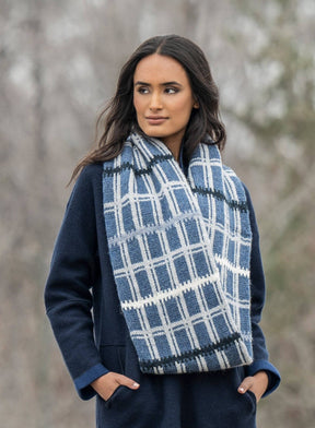 Wrapped in the Blue Sky Fibers Aurora Infinity Cowl, a person stands outdoors. The natural woolly warmth of the cowl complements their dark blue coat and long dark hair, while softly blurred trees form the backdrop.